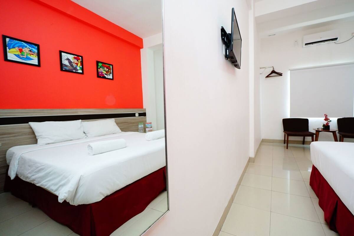 A hotel room with two beds, a TV mounted on the wall, a desk with a chair, and a window.