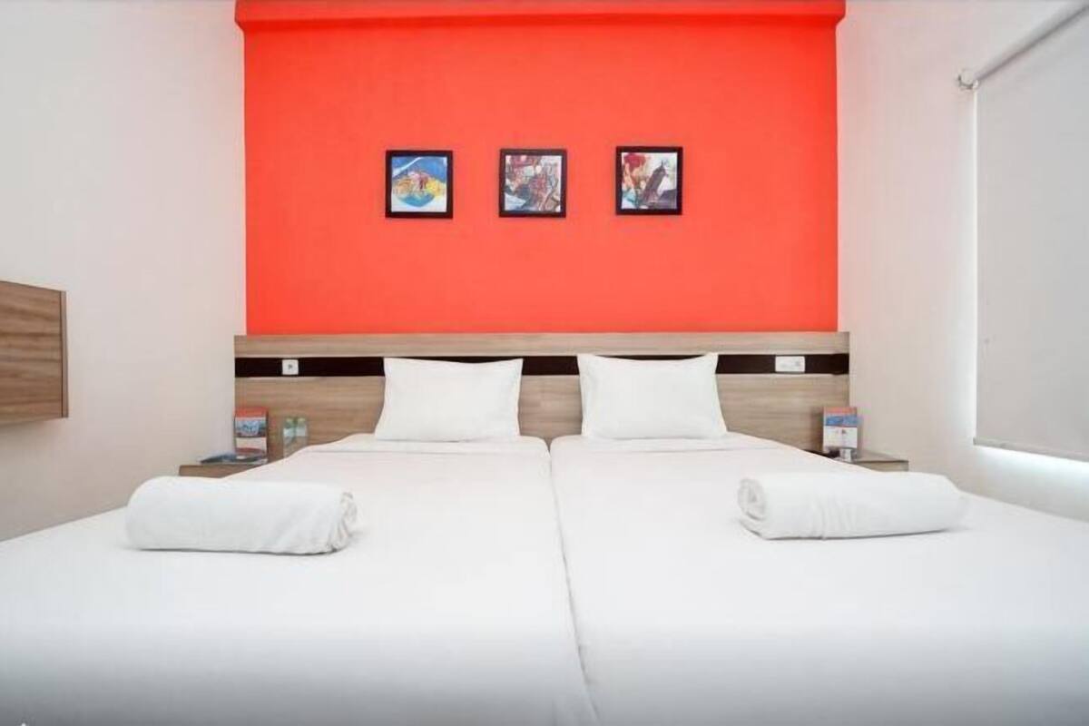 A hotel room with two beds, a red accent wall, and three framed pictures.