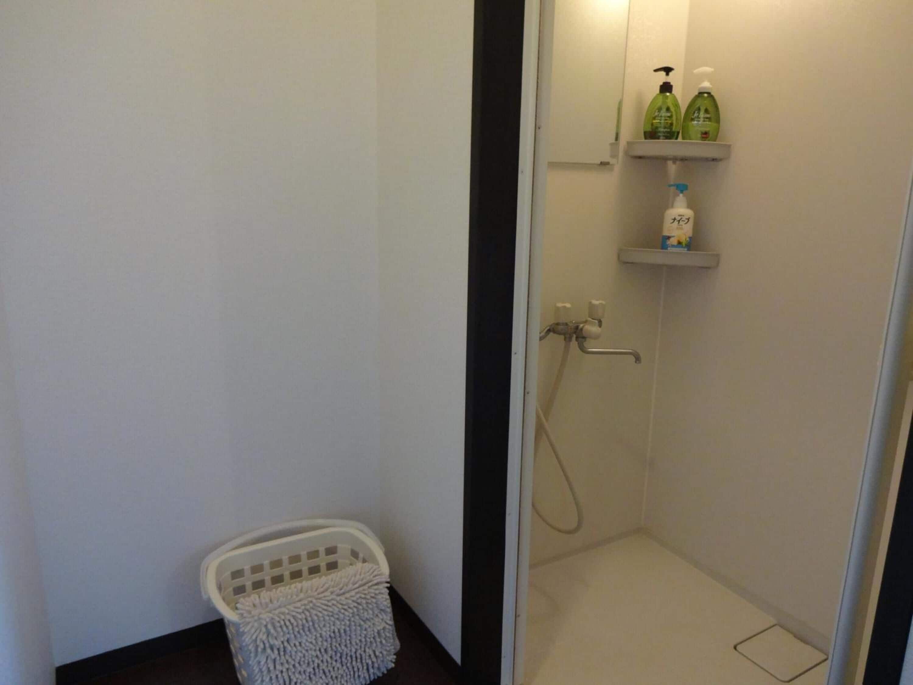 A small, clean bathroom with a shower, a white laundry basket, and shelves with toiletries.