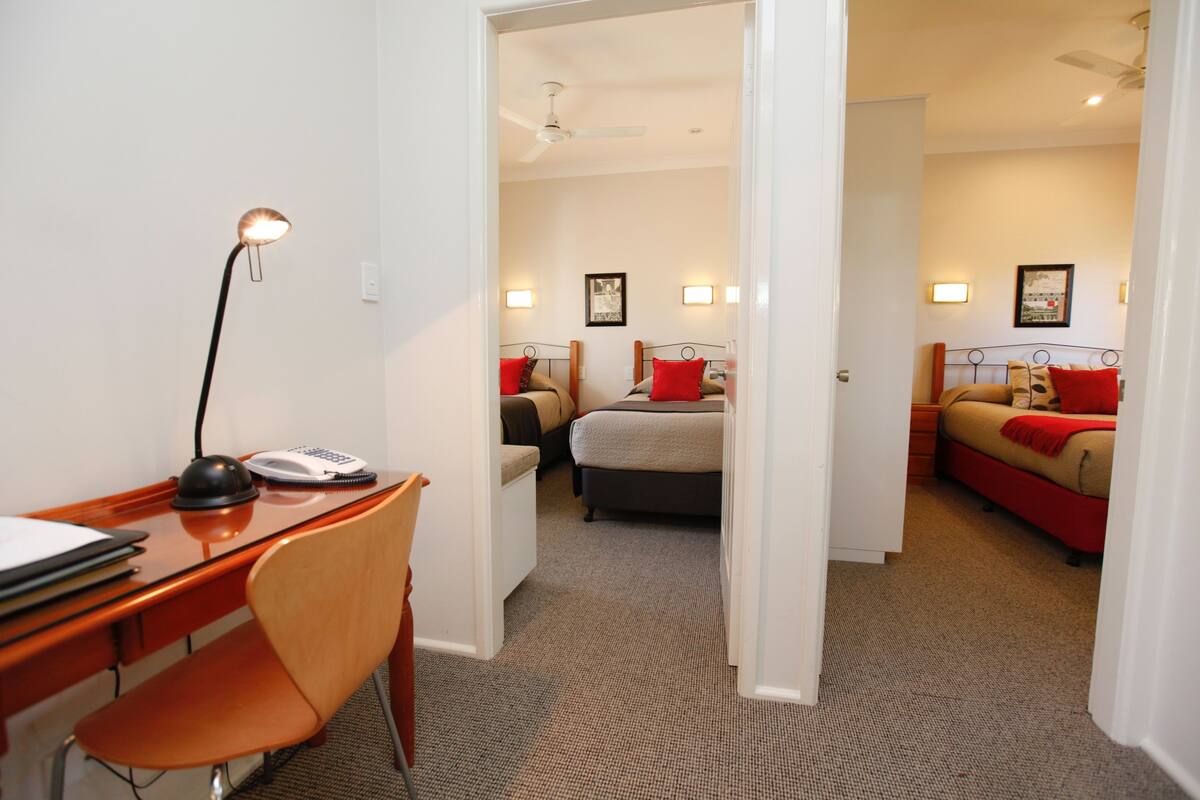 Ein Hotelzimmer mit Schreibtisch, Stuhl, zwei Betten und Deckenventilator.