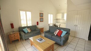 A living room with two grey sofas, a wooden coffee table, and a kitchen in the background. - Country Apartments (Dubbo)