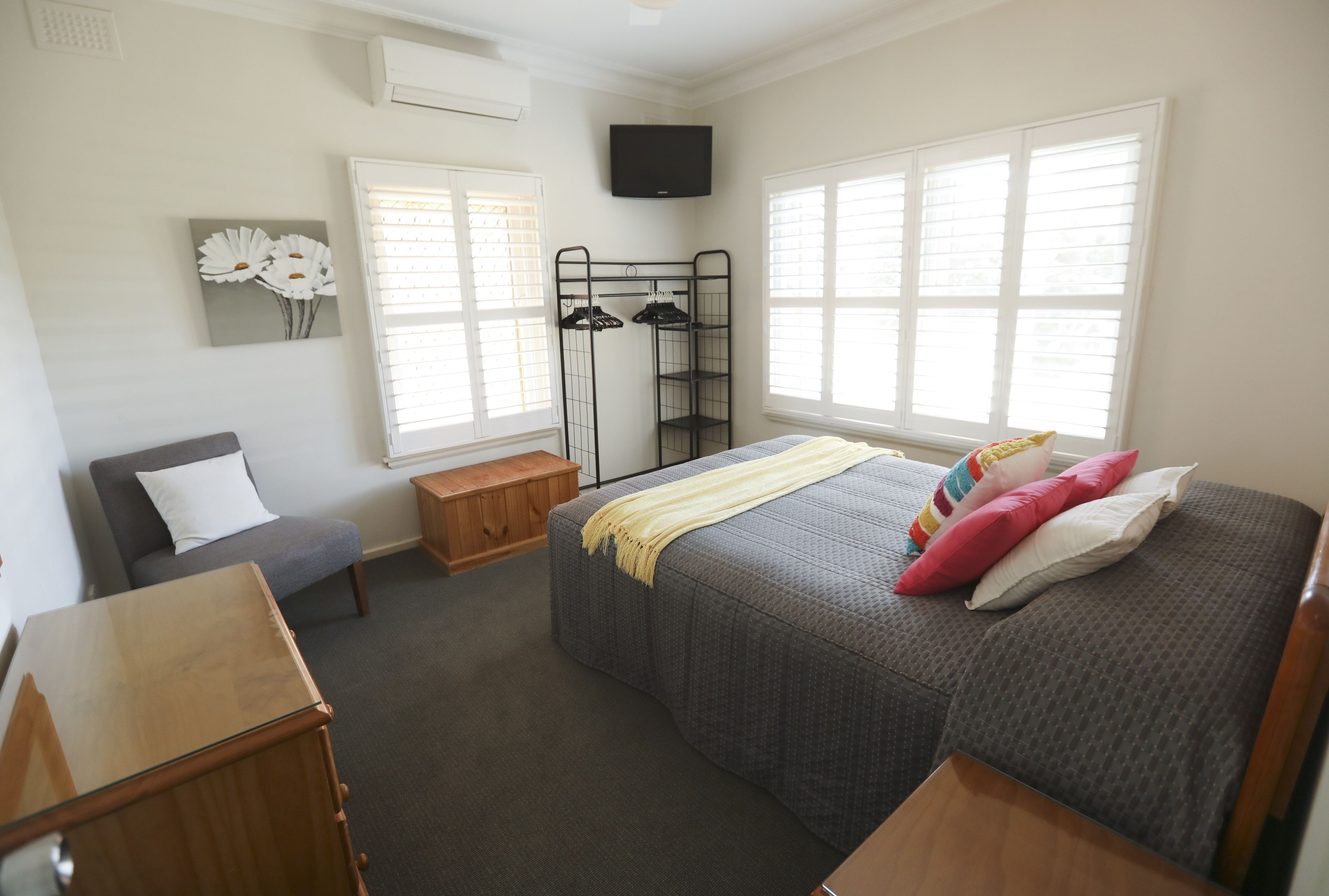 A bedroom with a bed, a chair, a wooden bench, a TV, and a window.