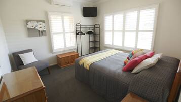 A bedroom with a bed, a chair, a wooden bench, a TV, and a window.