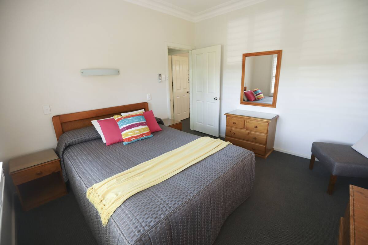 Ein Schlafzimmer mit einem Bett, einem Schminktisch, einer Bank, einem Spiegel und einer Tür.