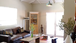 Een ruime woonkamer met een hoge plafond, een houten salontafel, een bruine leren bank en een decoratieve hanglamp.