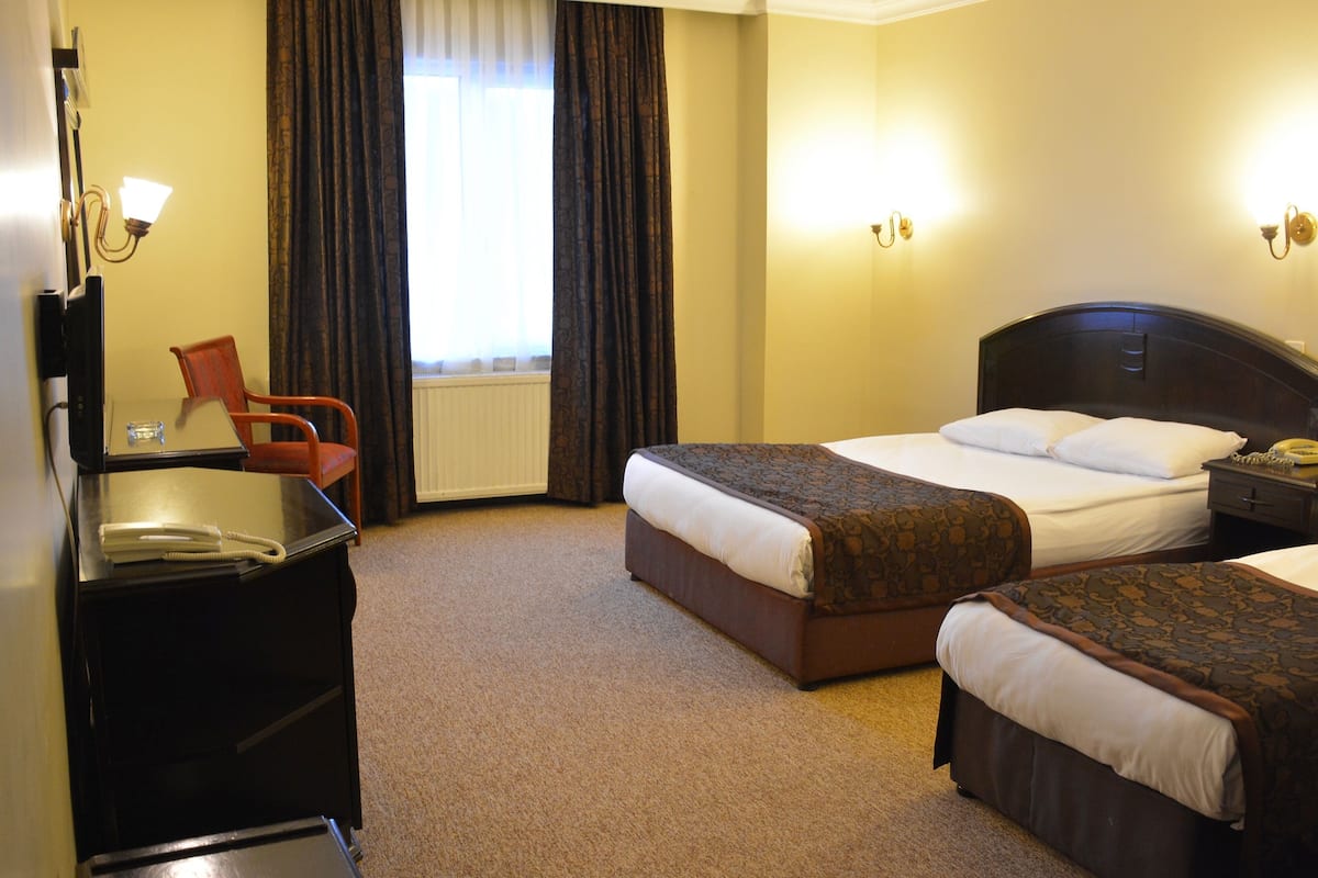 A hotel room with two beds, a desk, a chair, and a window with curtains.