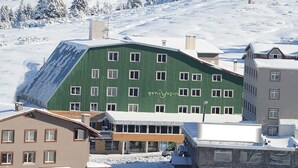 A hotel with a green facade, multiple windows, and a ski slope in the background. - Genc Yazici Hotel Uludag (Bursa)