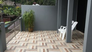 Eine überdachte Terrasse mit einem Rochenmuster-Boden, einem Blumentopf und weißen Kunststoffstühlen.