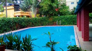 Une piscine entourée d’une végétation luxuriante et un bâtiment à la façade jaune.
