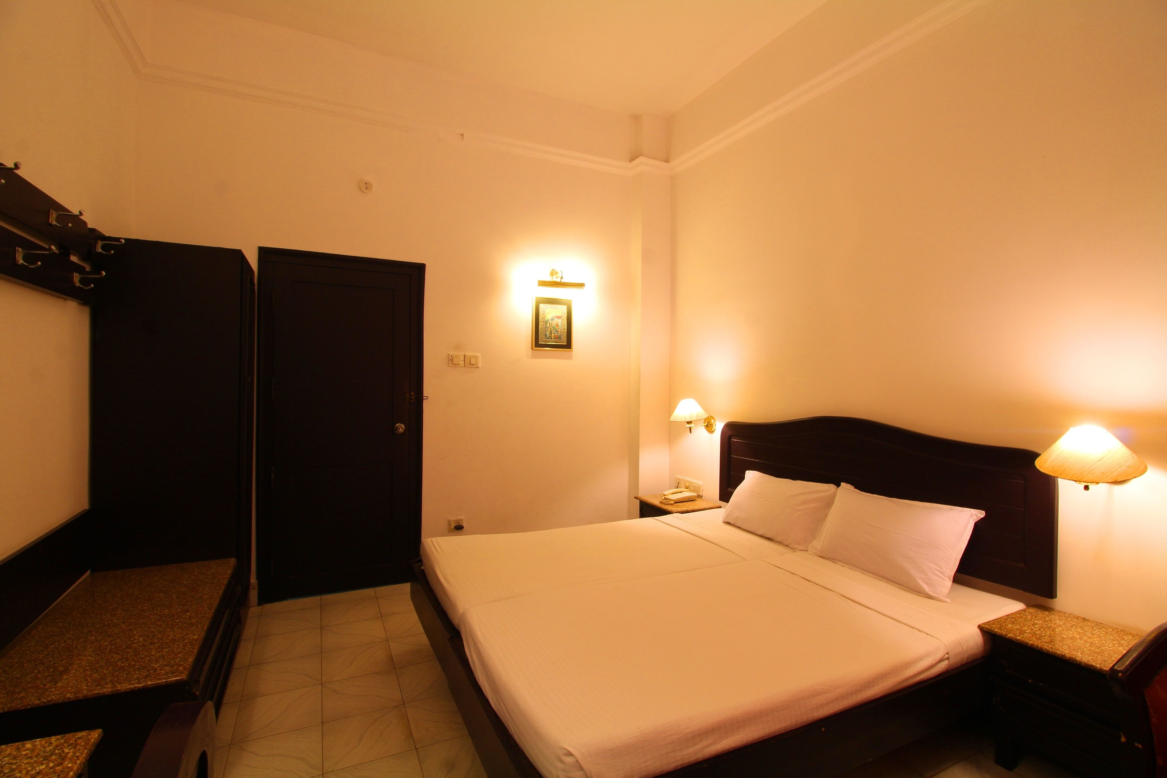 Habitación de hotel con cama, mesitas de noche, lámpara de pared y una puerta.