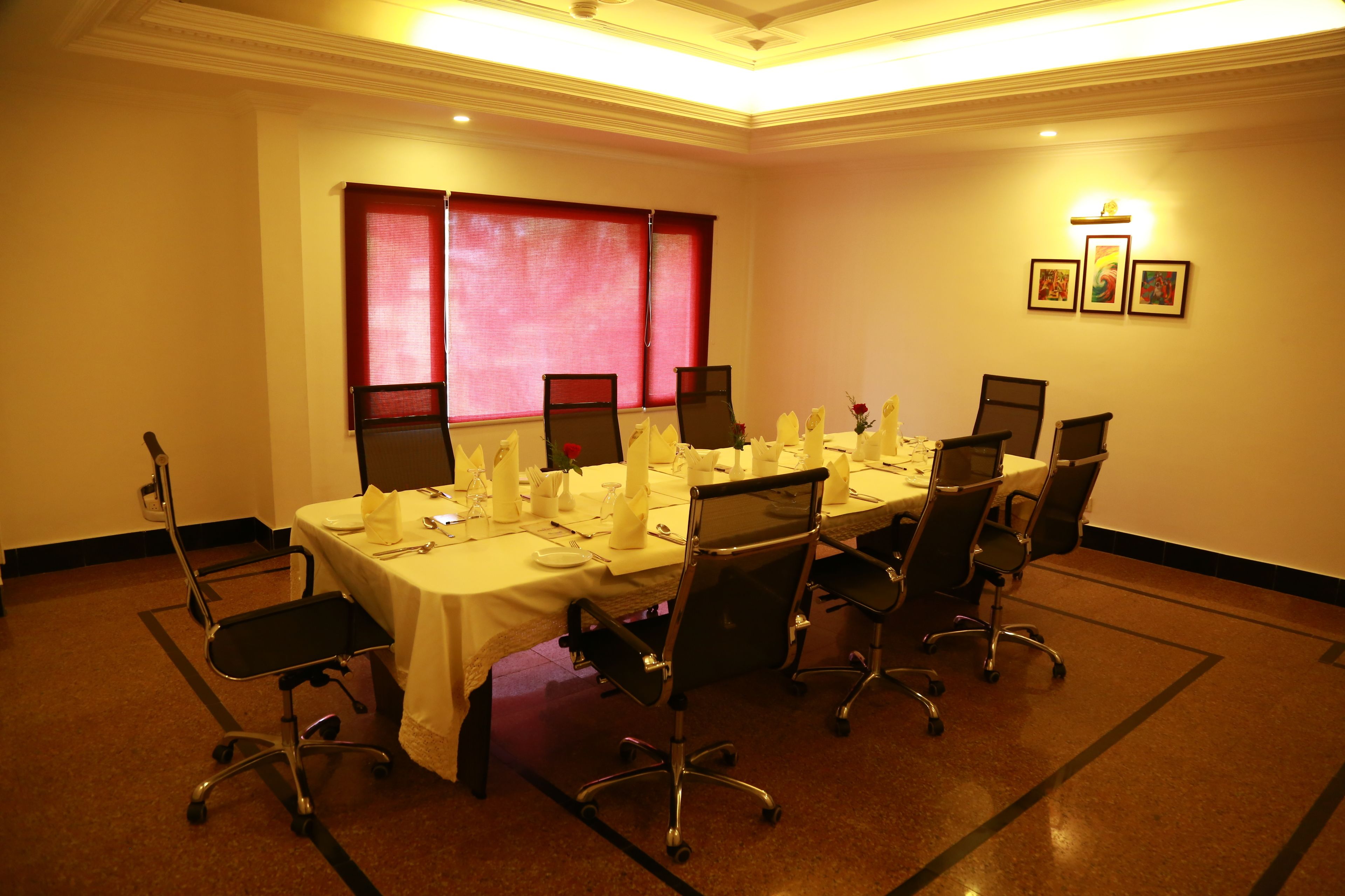 A conference room with a long table, multiple chairs, and a window with red curtains.