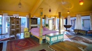 A spacious bedroom with a large bed, multiple rugs, and a view of the outdoors.