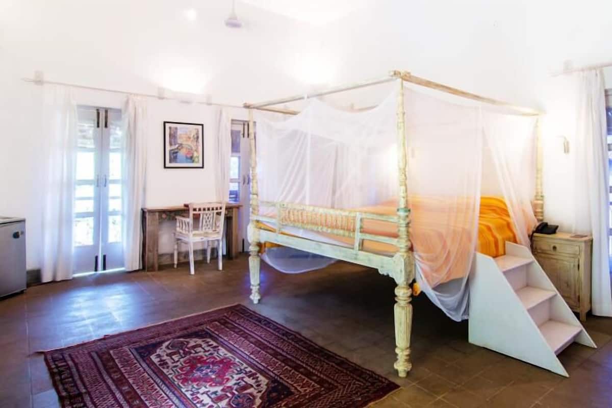 A four-poster bed with a canopy, a desk with a chair, and a large rug.
