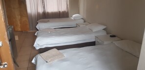 A hotel room with three beds, a small bedside table, and a door leading to a bathroom.