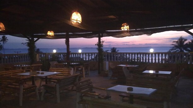 An outdoor seating area with tables and benches, overlooking a body of water during twilight.