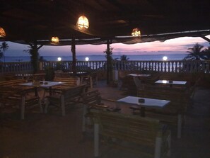 An outdoor seating area with tables and benches, overlooking a body of water during twilight. - Hotel Panorama (Tanjung Pinang)