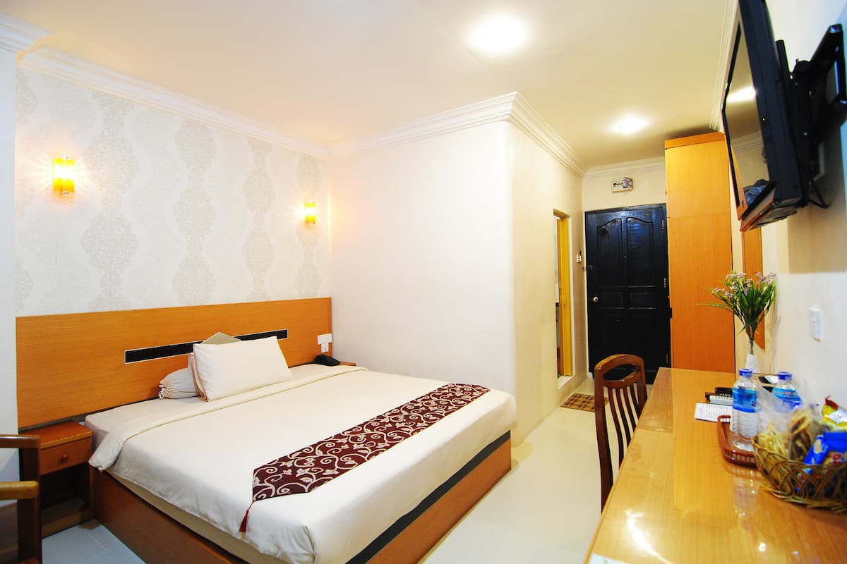 A hotel room with a bed, bedside table, lamp, and a dining table with chairs.
