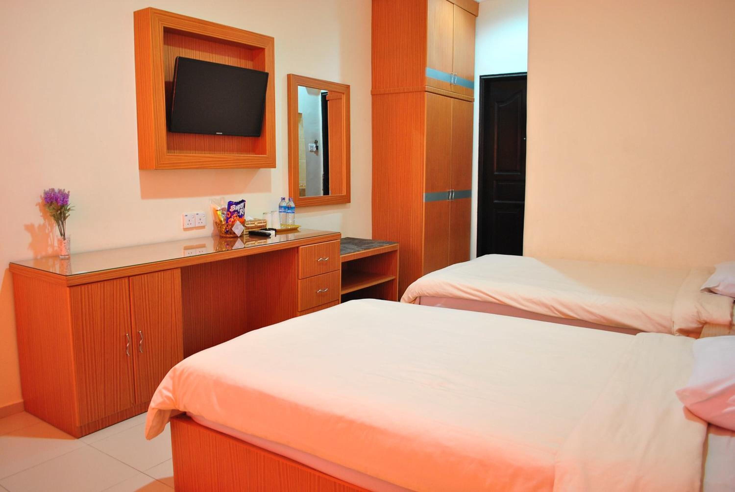 A hotel room with two beds, a wooden dresser, a television, and a mirror.