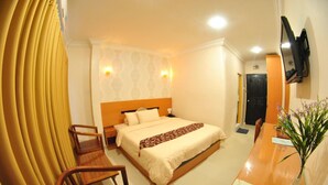 A hotel room with a bed, wooden chairs, a desk, a TV, and a vase with flowers.