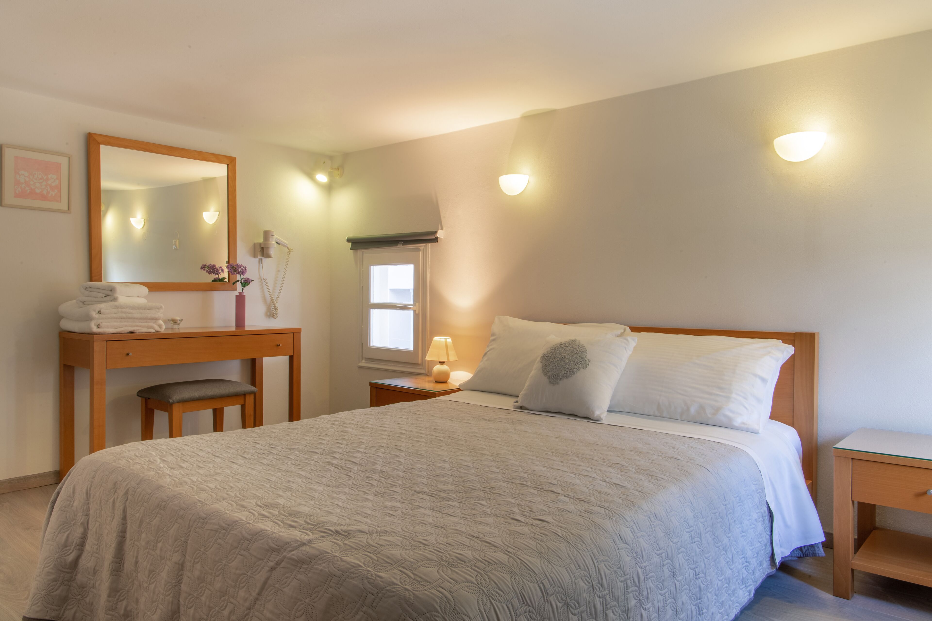Een slaapkamer met een bed, een bureau, een stoel, een nachtkastje en een bedtafeltje.