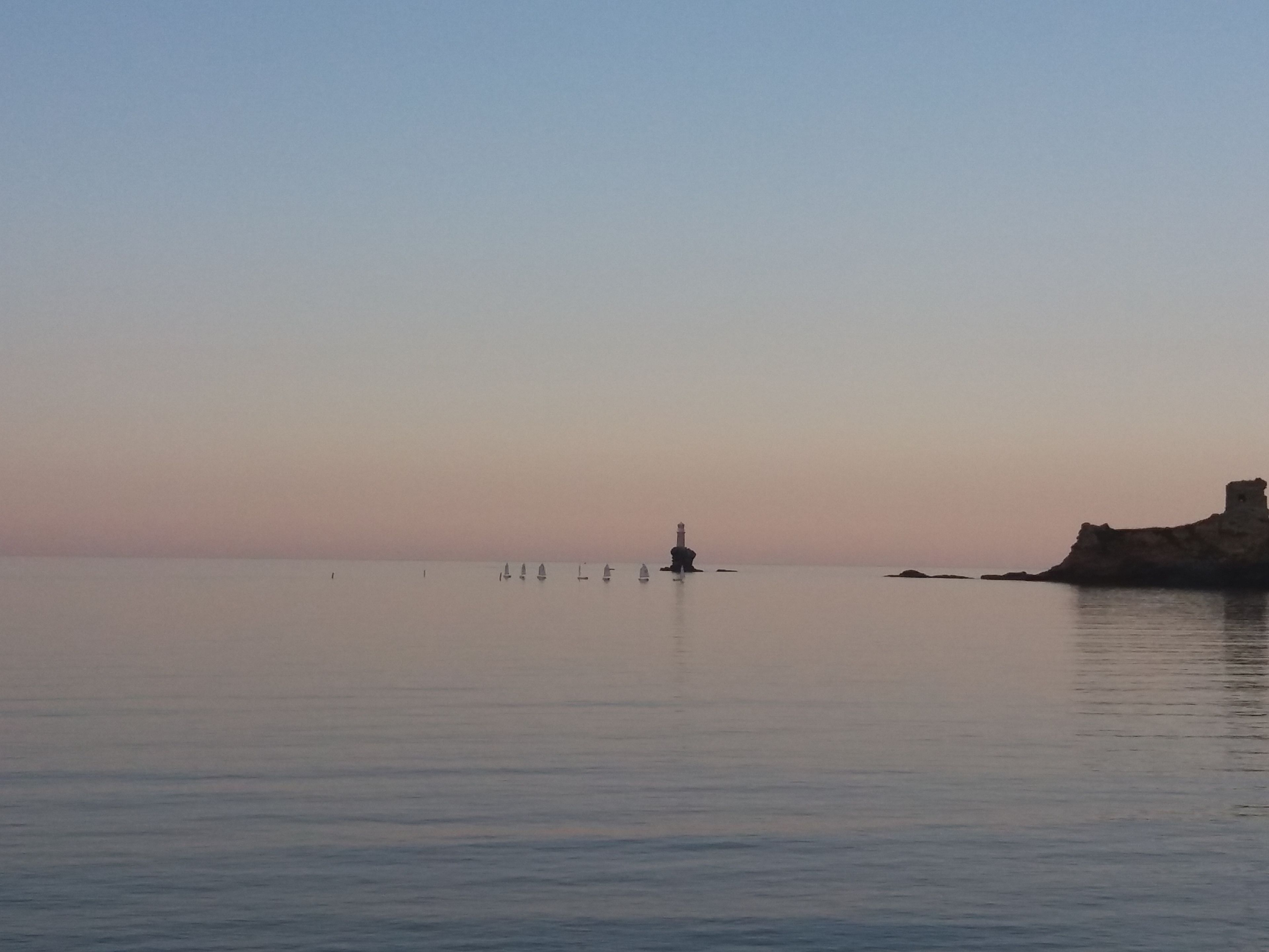 Un mar tranquilo con un faro y afloramientos rocosos.