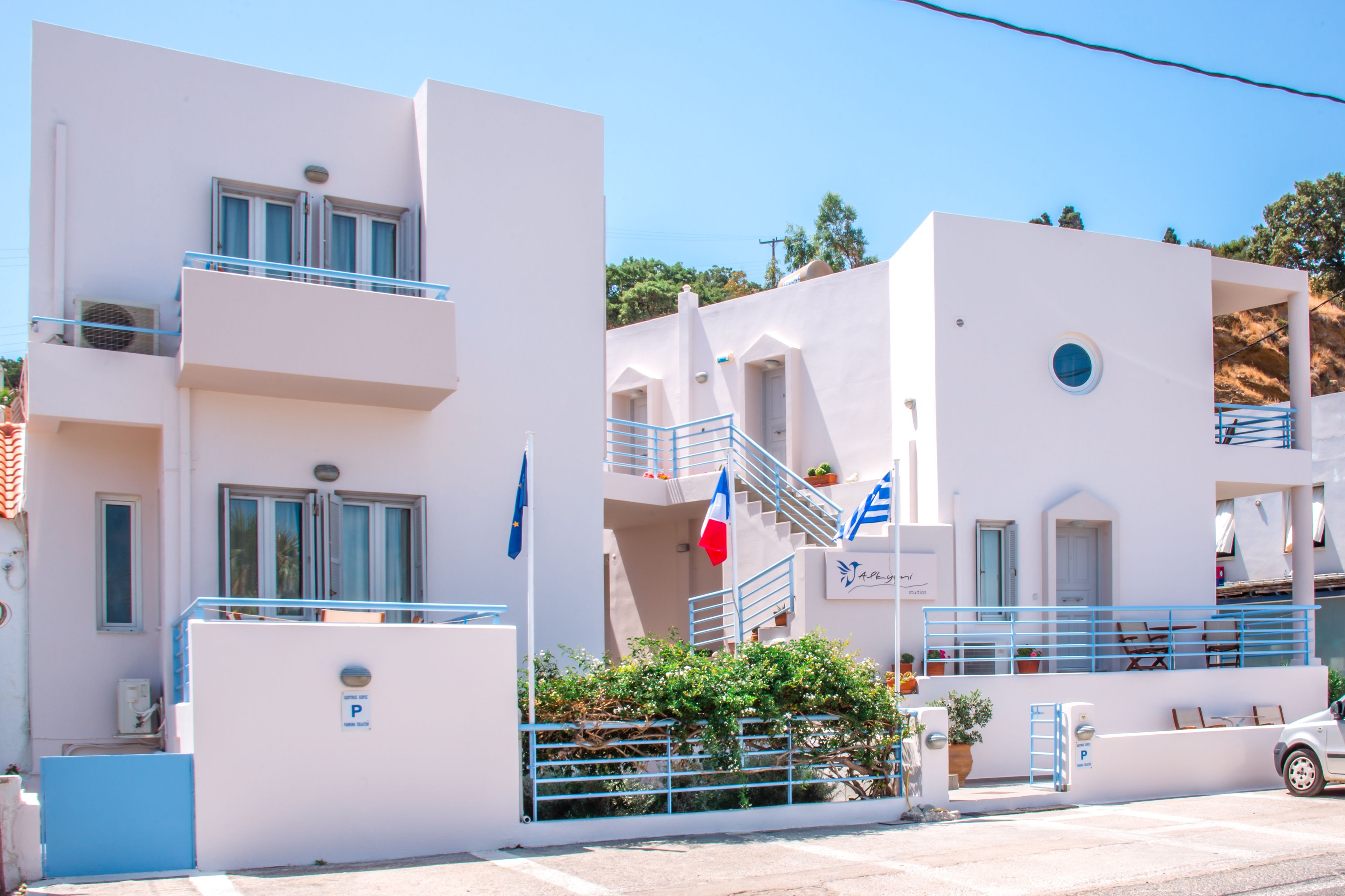 A white building with balconies, a staircase, and a parking sign.