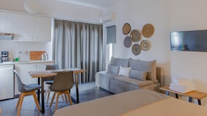 Una habitación de hotel moderna con una cama, un sofá, un área de comedor con sillas, una pequeña cocina y un televisor montado en la pared.