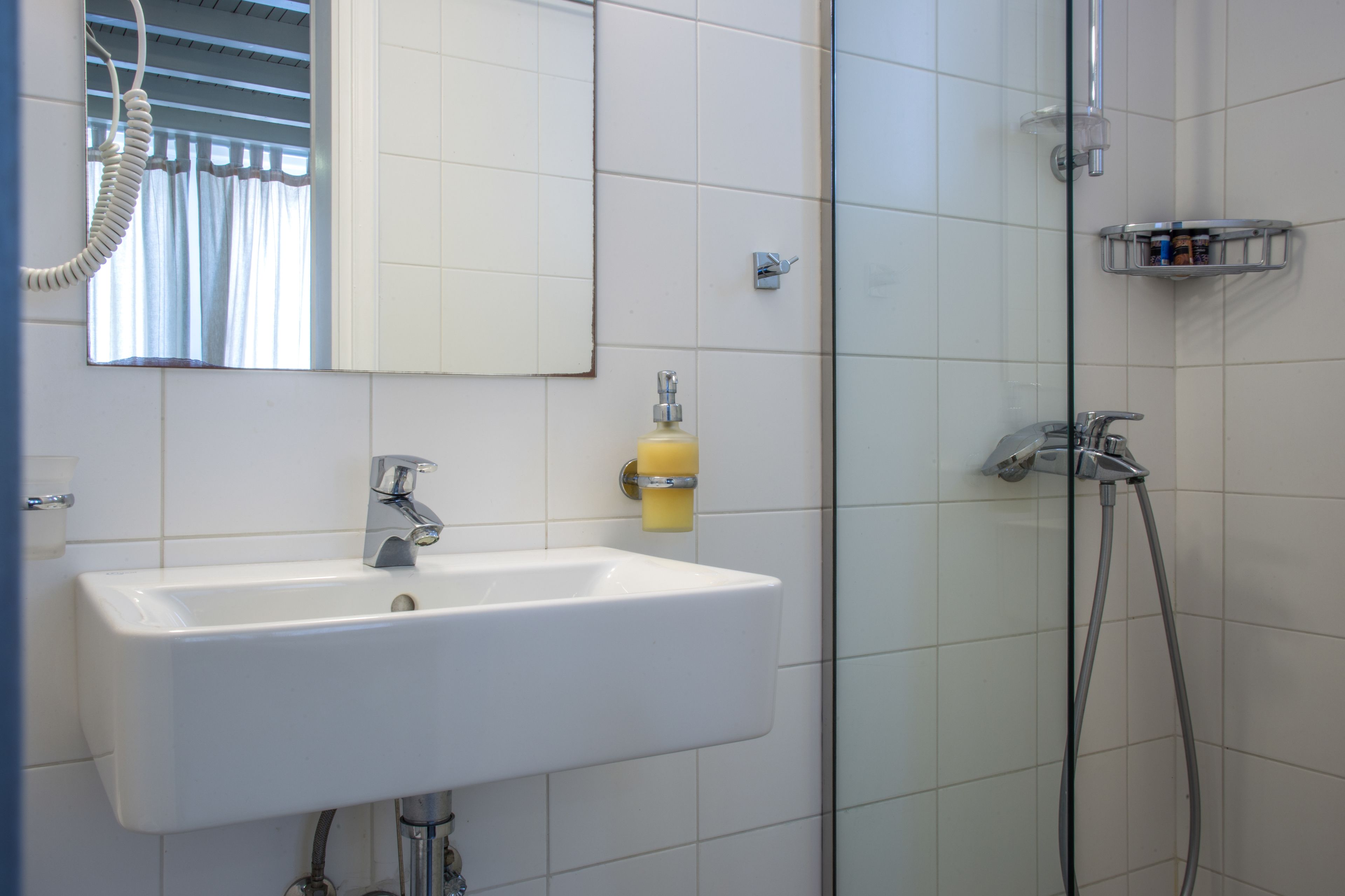 Une salle de bain avec un lavabo blanc, un miroir et une douche.