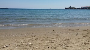 Una playa con agua cristalina, un faro distante y un promontorio rocoso con edificios.