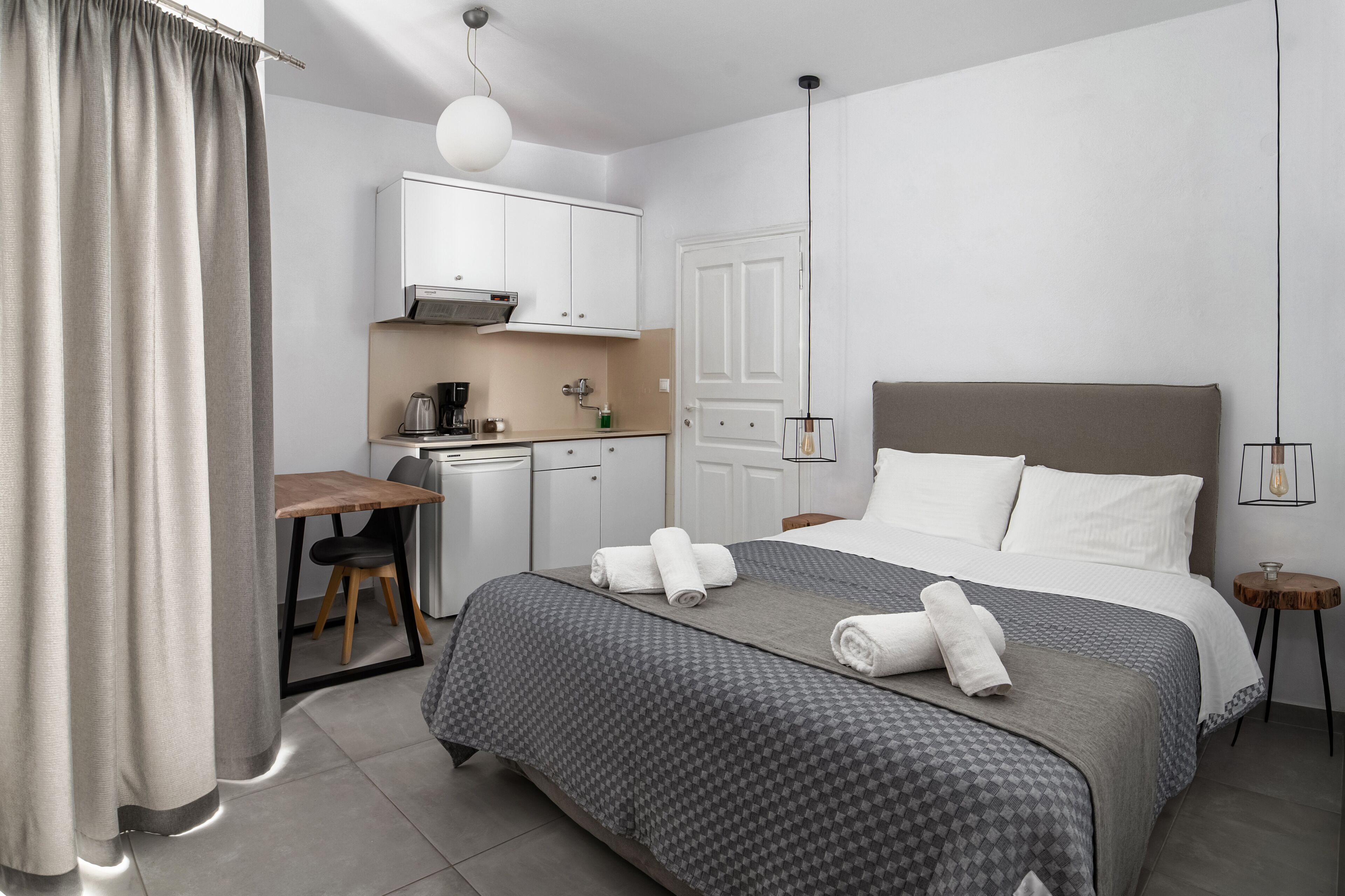 Una habitación de hotel moderna con cama, mesita de noche y una zona de kitchenette.