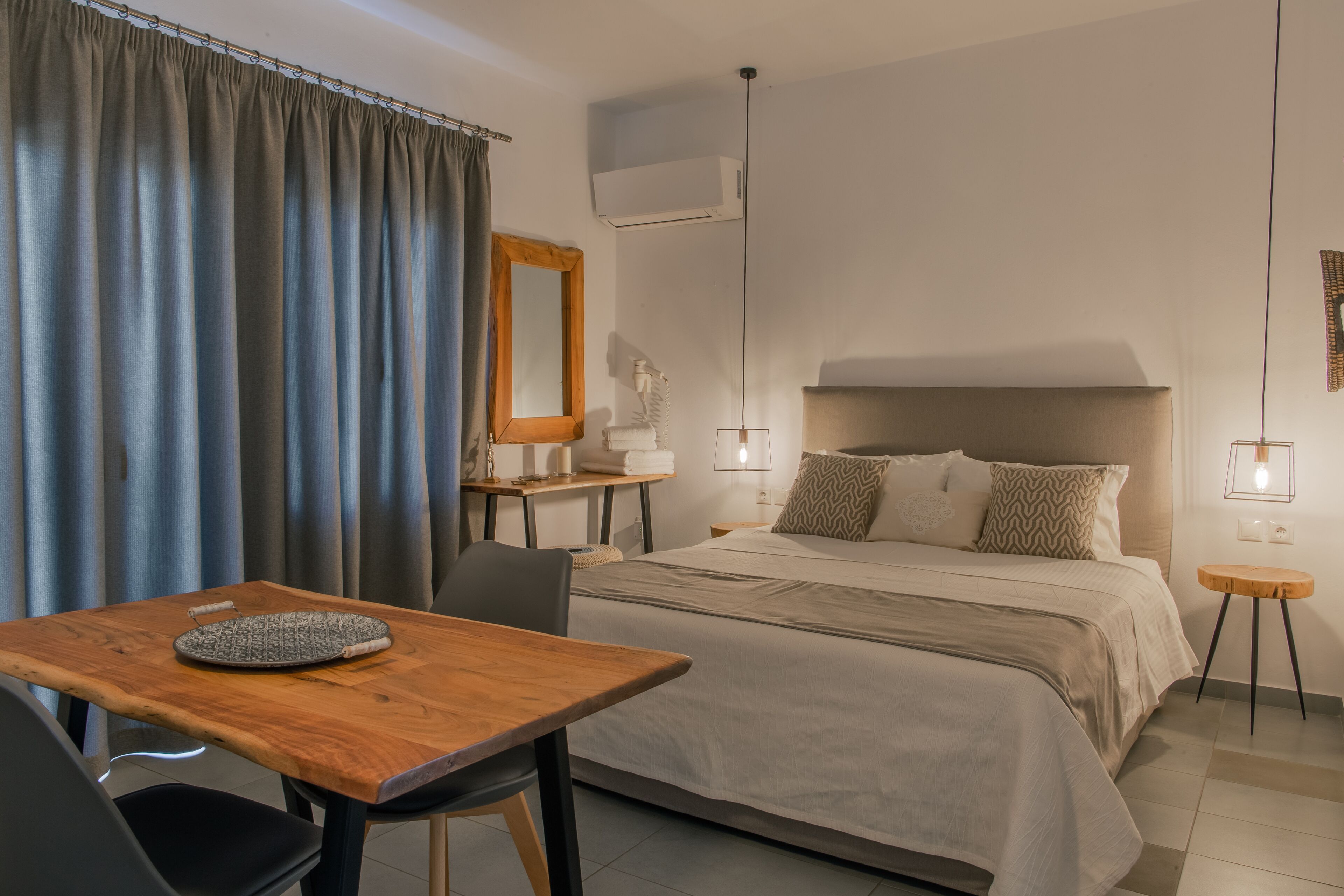 Une chambre d’hôtel comprenant un lit, une table en bois, une chaise, un bureau, un miroir, une lampe et un climatiseur.