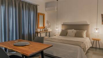 Une chambre d’hôtel comprenant un lit, une table en bois, une chaise, un bureau, un miroir, une lampe et un climatiseur.