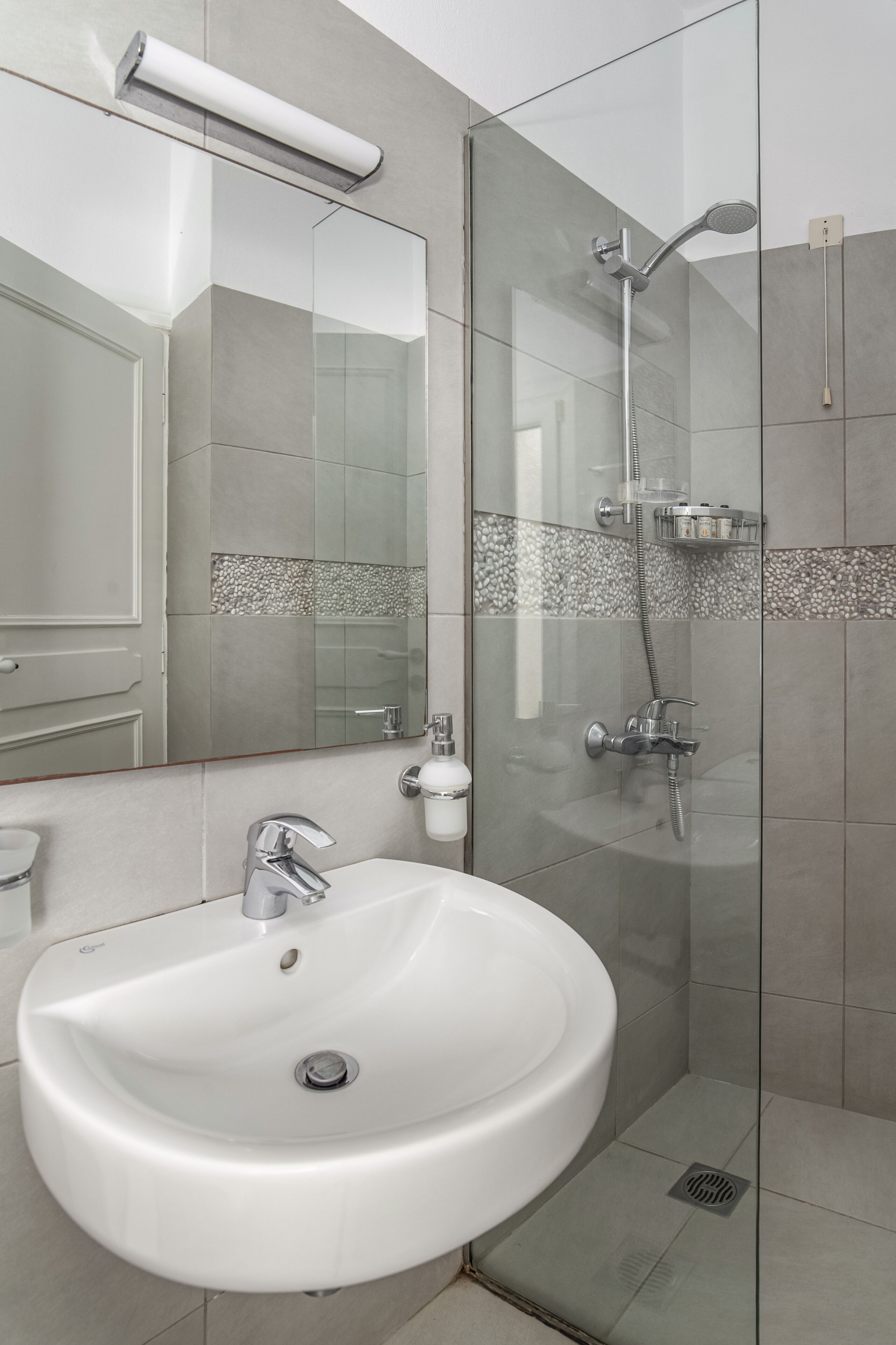 Een moderne badkamer met een wit wastafelmeubel, een douchecabine van glas en een spiegel boven het wastafelmeubel.