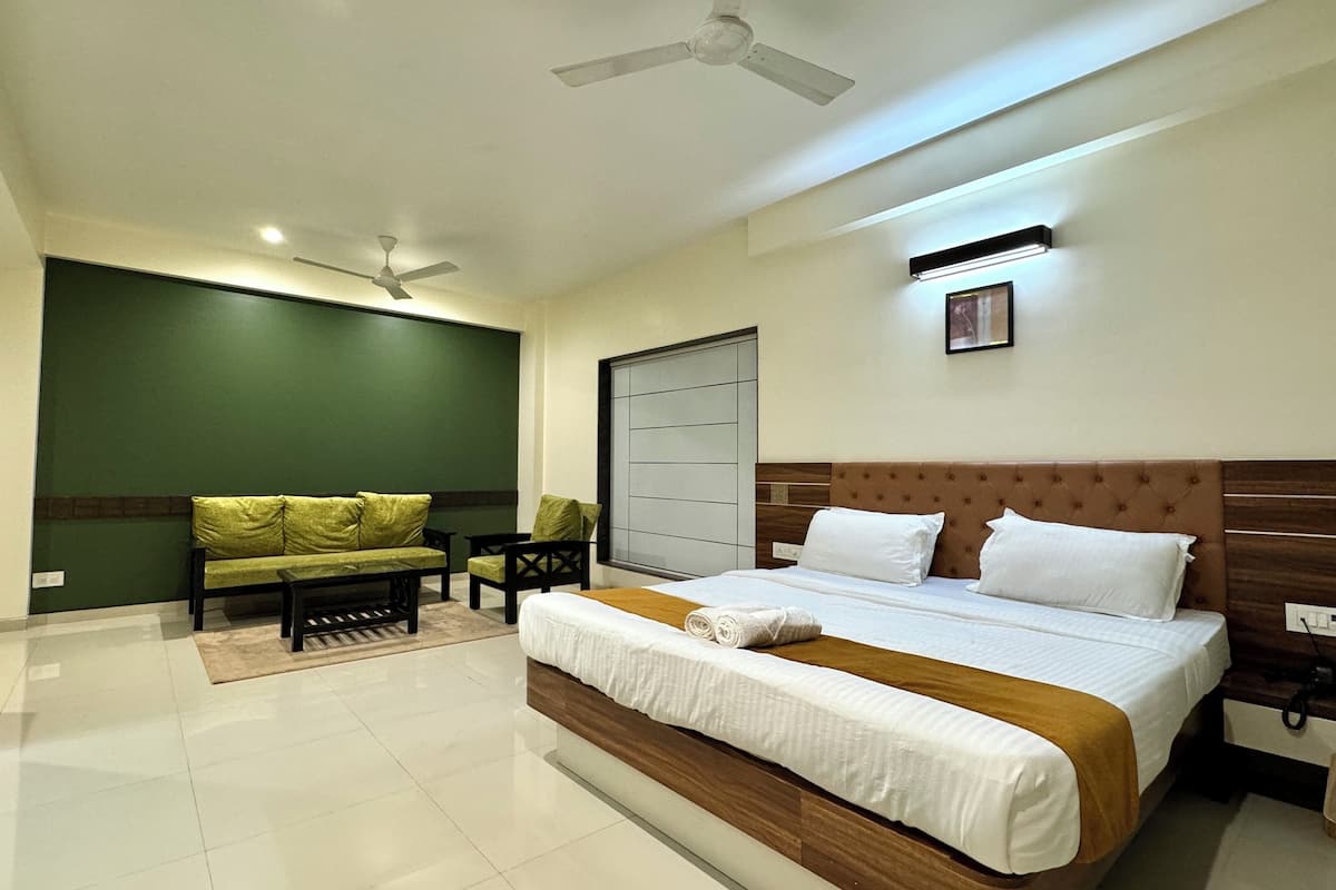 A hotel room with a bed, a sofa, a chair, a ceiling fan, and a wall-mounted light.
