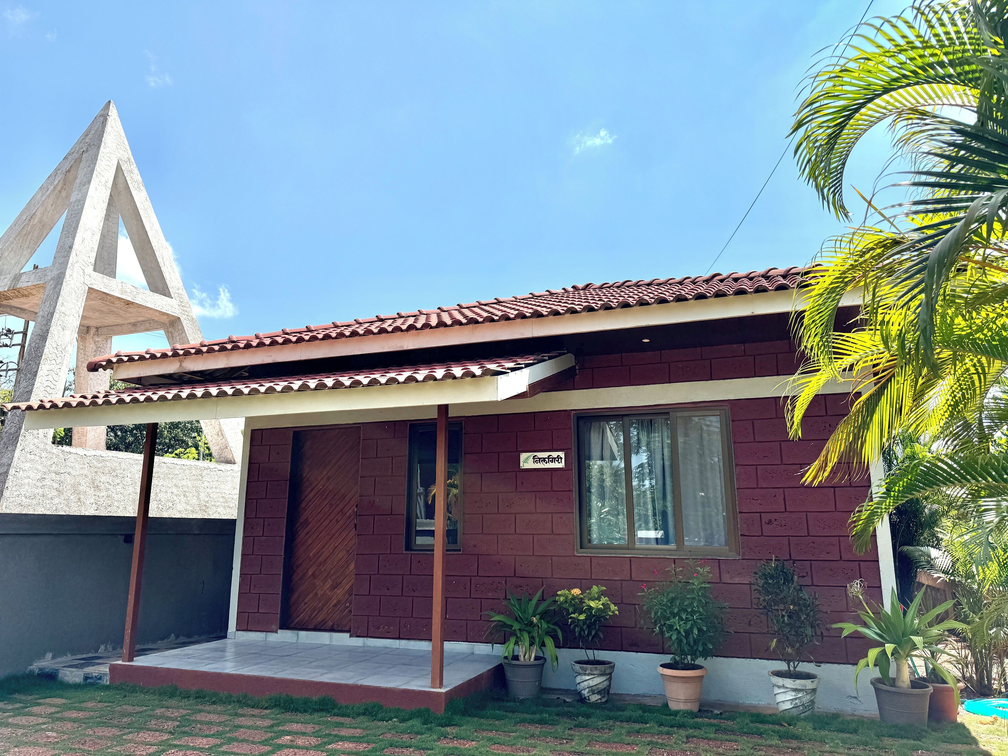 Een huis met een pannendak, bakstenen muren en een overdekte veranda. Voor het huis staan potplanten.