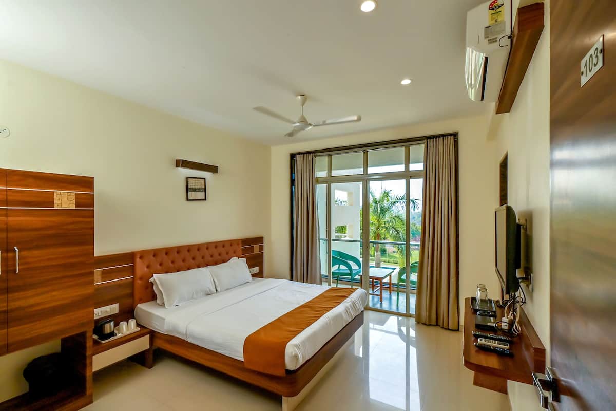 A hotel room with a bed, a TV, a ceiling fan, and a balcony with a table and chairs.