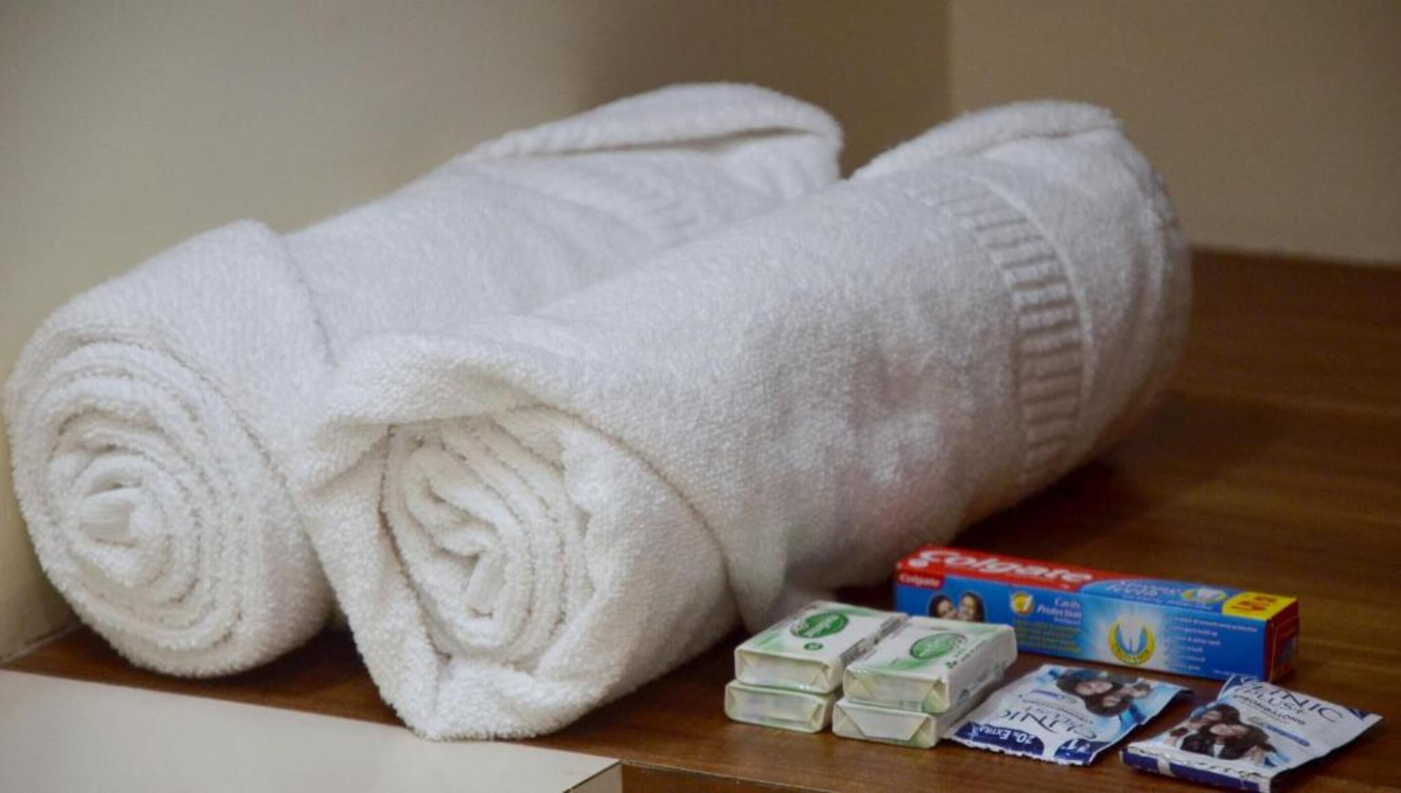 Two rolled white towels, a box of Crest toothpaste, and several packs of Marlboro cigarettes on a wooden surface.