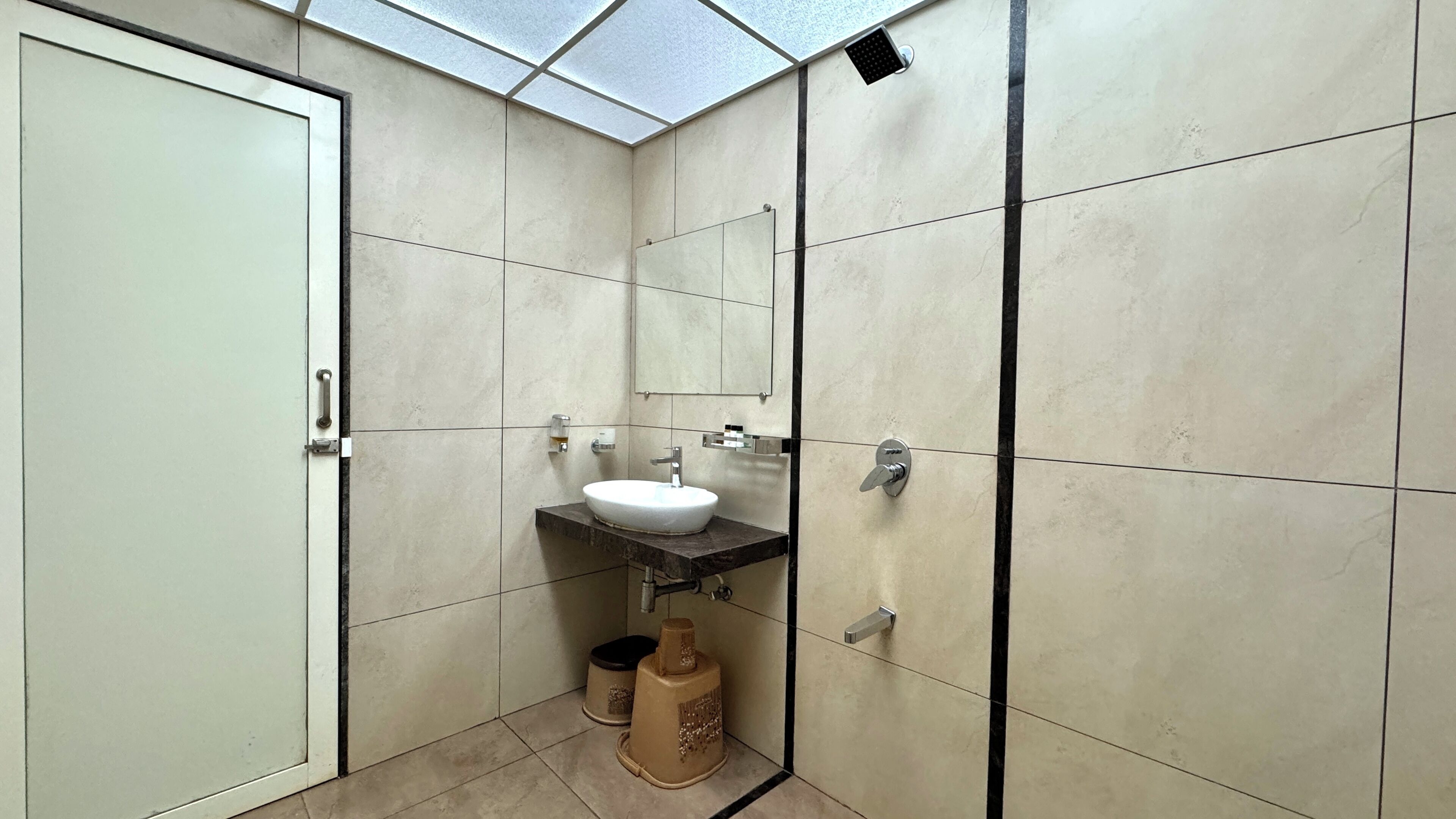 A bathroom with a white door, a sink, a mirror, and a shower area.