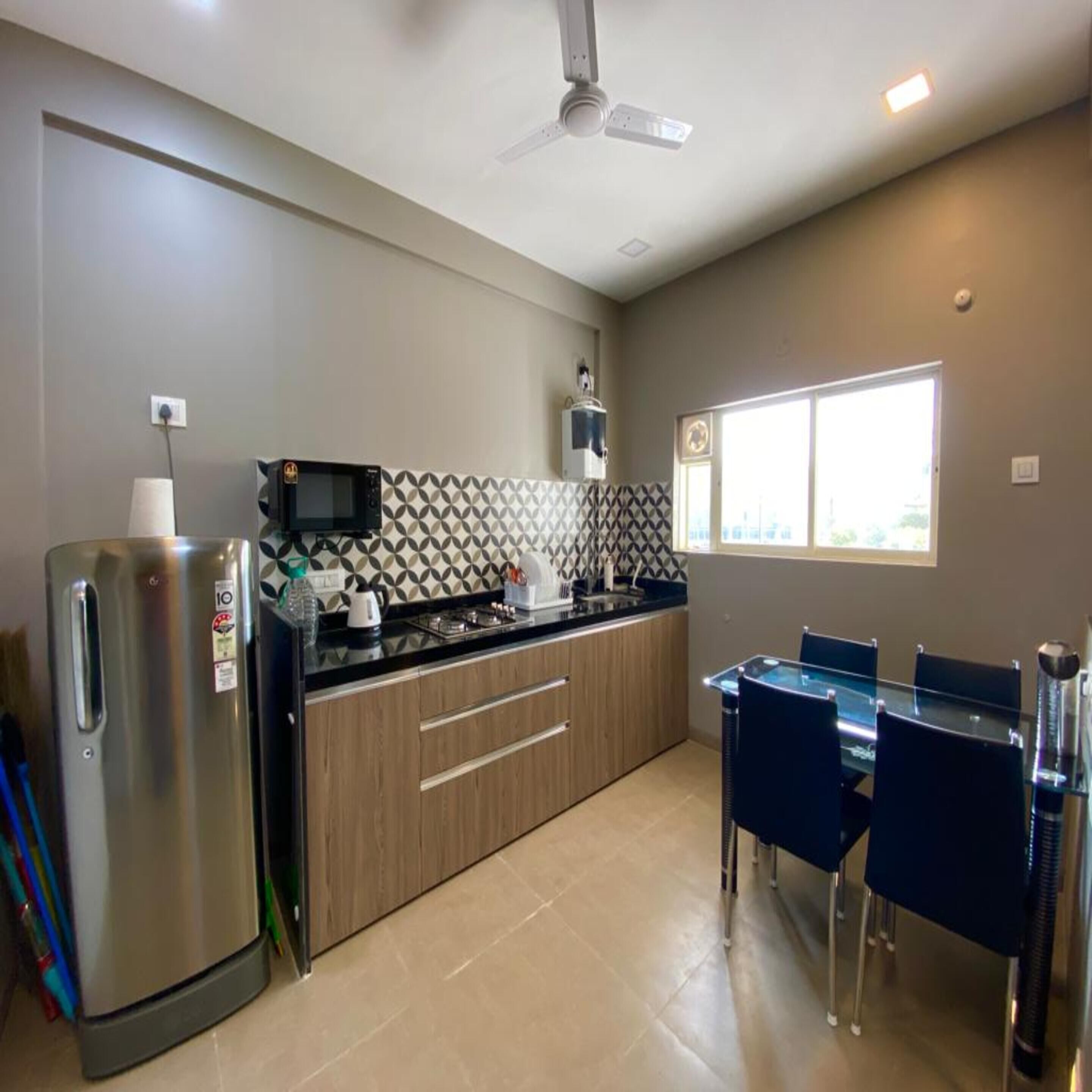 A compact kitchen with a refrigerator, microwave, and stove. There is a dining table with chairs and a window providing natural light.