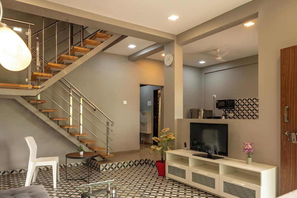 A modern living room with a staircase, a flat-screen TV, and a potted plant.