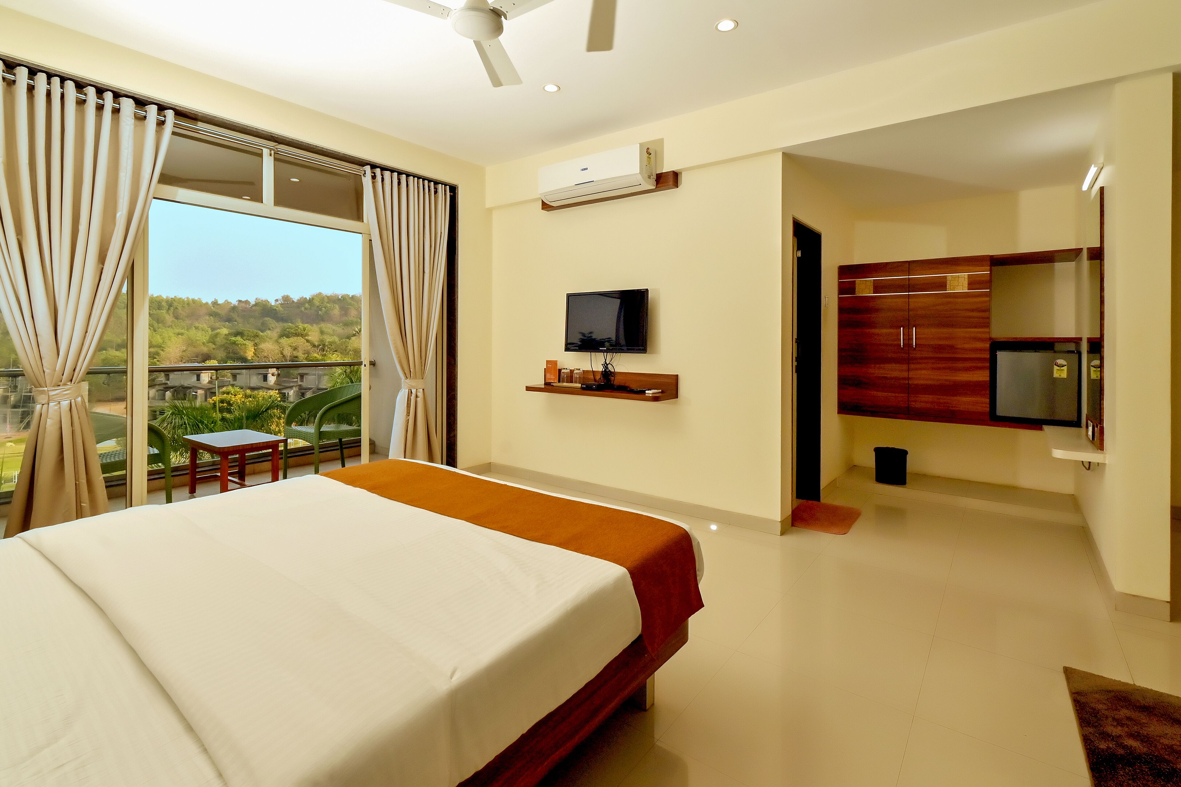 Une chambre d’hôtel avec un grand lit, un téléviseur fixé au mur, un balcon avec des rideaux et une vue sur la verdure environnante.