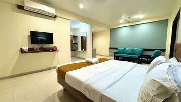 A hotel room with a bed, a TV, a sofa, and a bathroom visible through an open door.