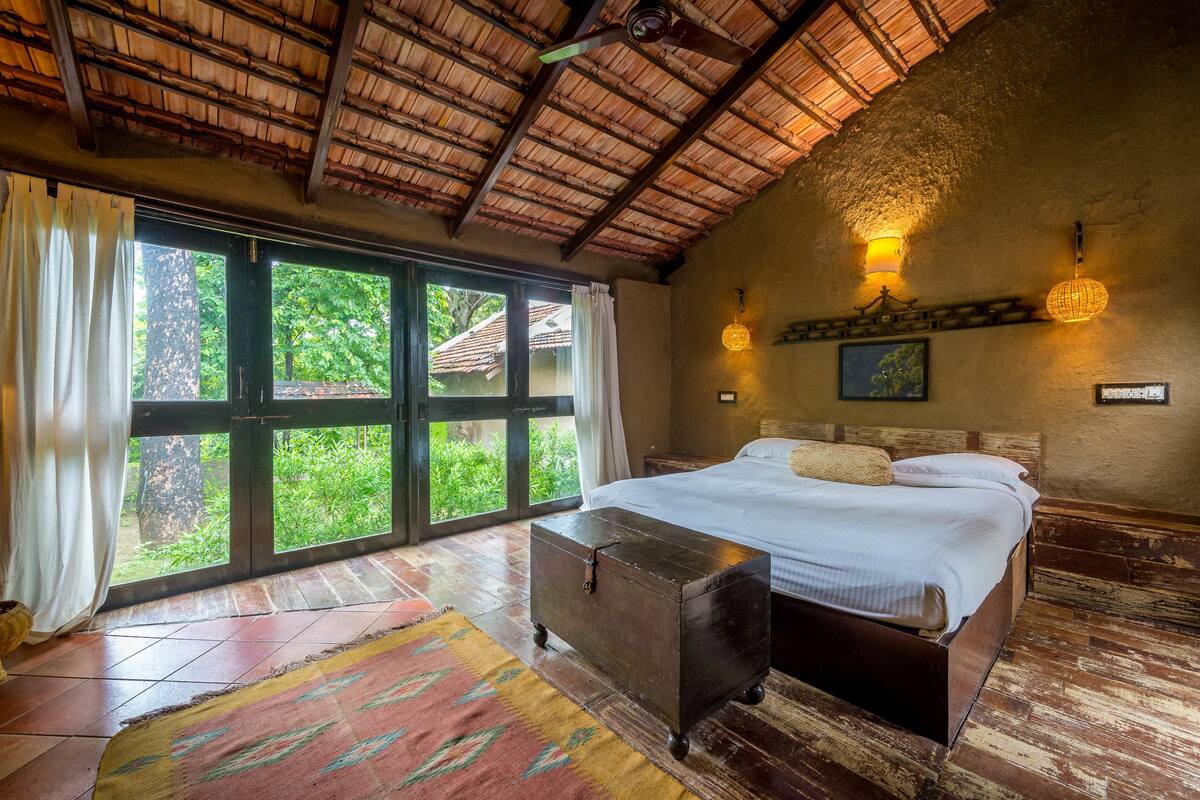 Un dormitorio espacioso con una cama grande, un cofre de madera y vistas a la vegetación a través de una puerta corredera.