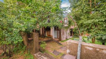 A rustic garden with stone steps leading to a wooden door, surrounded by lush greenery and hanging lanterns.