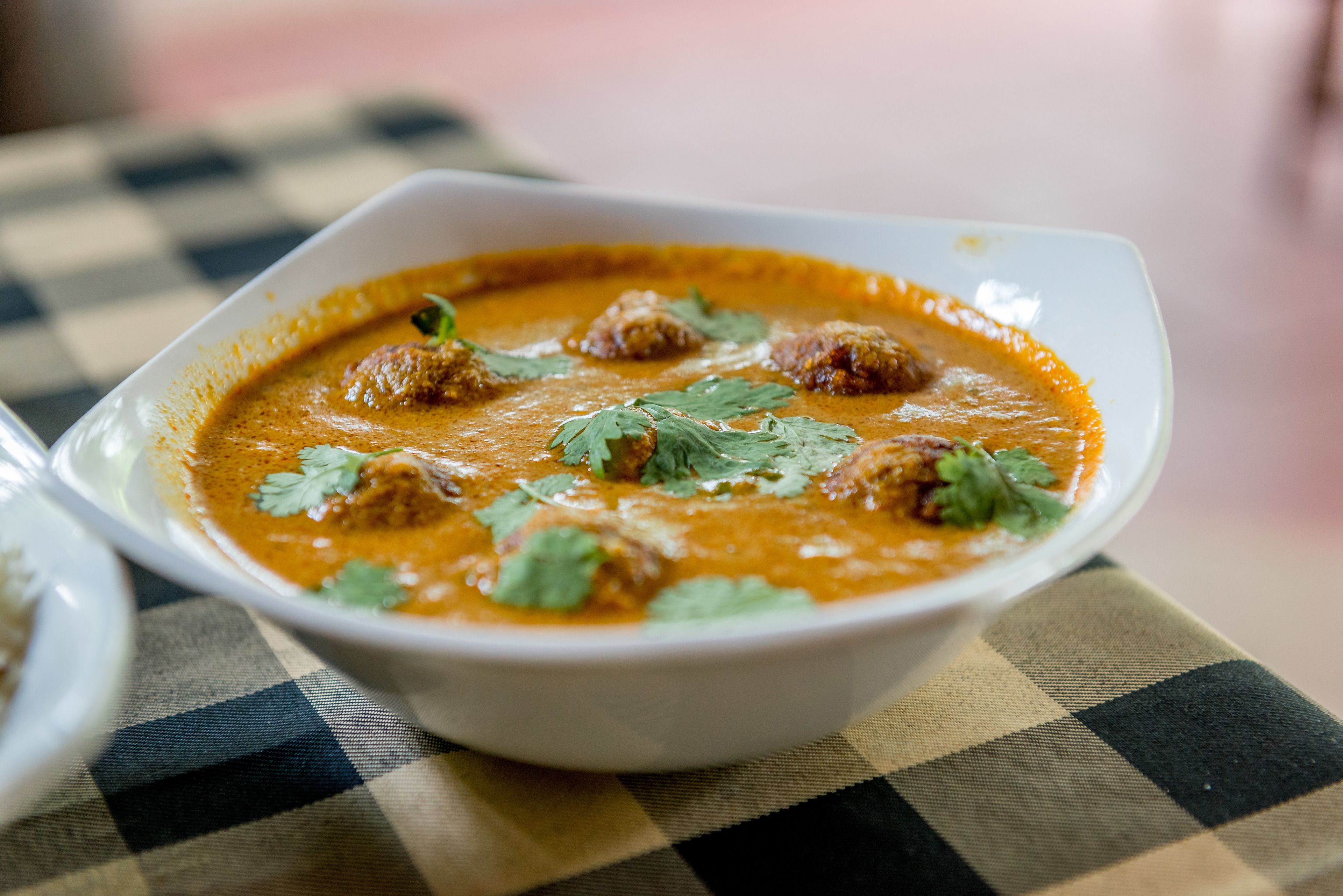 Un tazón de curry con albóndigas y cilantro como decoración sobre un mantel a cuadros.