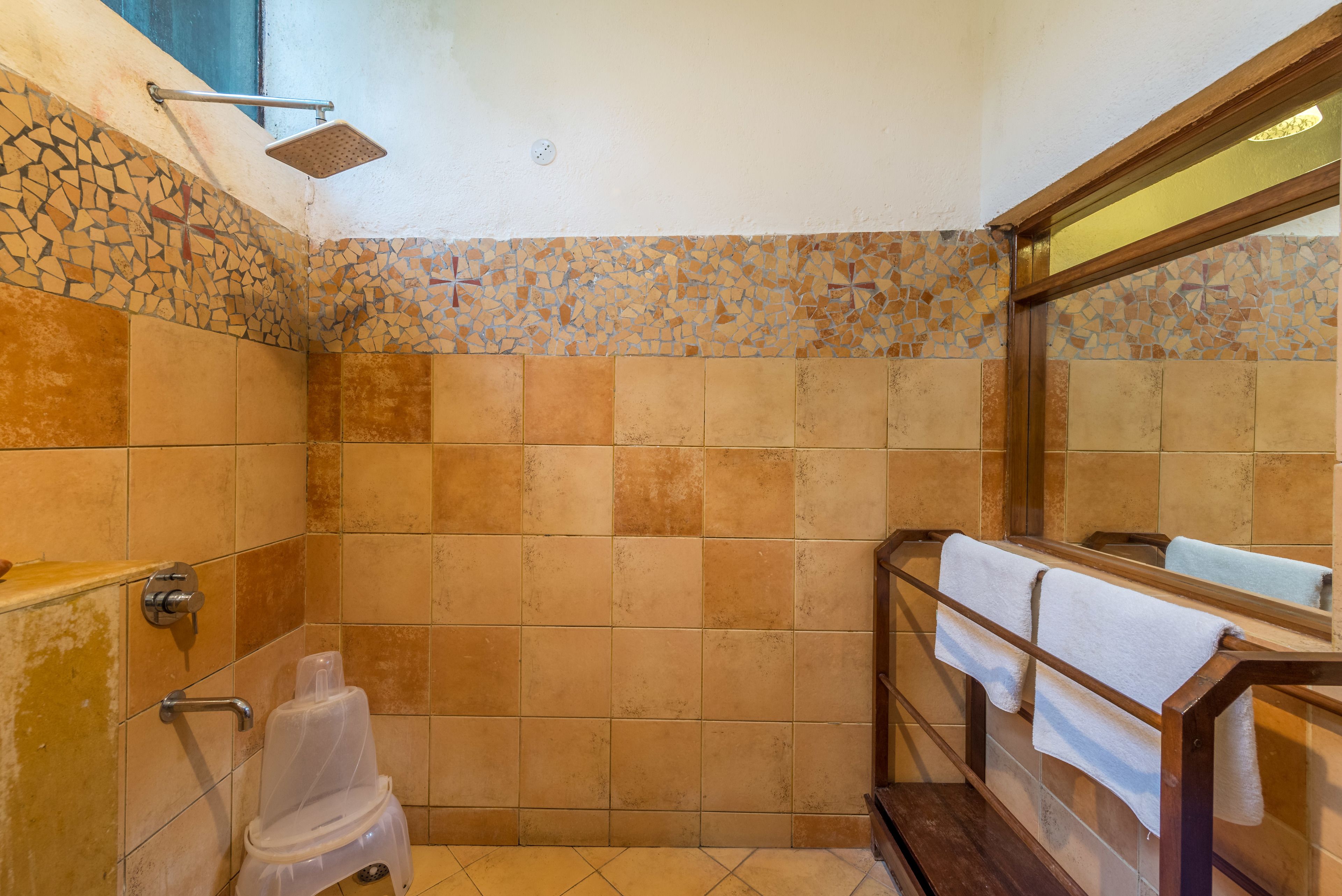 A bathroom with mosaic tile walls, a shower, a toilet, and a bench with towels.