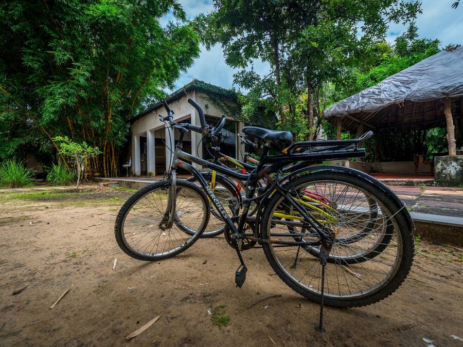 A bicycle parked on a dirt path with a building and trees in the background.
