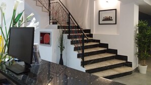 Una escalera moderna con barandilla de metal negro, una obra enmarcada en la pared y una planta en maceta junto a las escaleras.