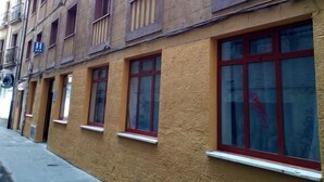 Un edificio de varios pisos con fachada amarilla, varias ventanas con marcos rojos y balcones.