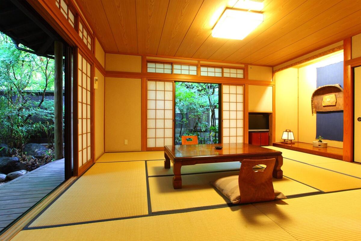 A traditional Japanese room with tatami flooring, a low table, and sliding doors leading to a garden.